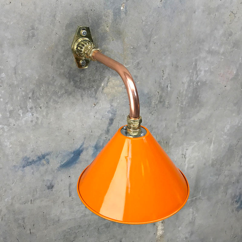An orange cantilever wall light with copper and brass wall fixture. The orange lamp shade is based on the design of the British military festoon shades. Colourful industrial style wall lights for contemporary interiors. 