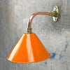 An orange cantilever light with copper and brass wall fixture. The orange lamp shade is based on the design of the British military festoon shades. Colourful industrial style wall lights for contemporary interiors.