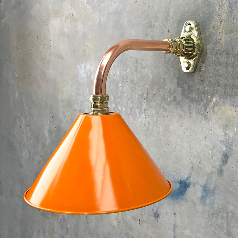 An orange cantilever wall light with copper and brass wall fixture. The orange lamp shade is based on the design of the British military festoon shades. Colourful industrial style wall lights for contemporary interiors. 