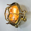 Solid brass industrial bulkhead light also called a bullseye lamp due to protective cage is reclaimed from nautical environments
