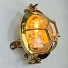 Solid brass industrial bulkhead light also called a bullseye lamp due to protective cage is reclaimed from nautical environments