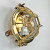 Solid brass industrial bulkhead light also called a bullseye lamp due to protective cage is reclaimed from nautical environments