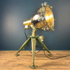 Shop for an industrial floor lamp. Comprised of a searchlight which has been expertly modified to integrate seamlessly with the USA military tripod, secured by three brass thumb screws for stability and functionality. A cast brass Wiska rotary marine isolator switch provides a reliable and straightforward mechanism for operating the lamp.