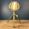 Shop for an industrial floor lamp. Comprised of a directional aluminium searchlight which has been expertly modified to integrate seamlessly with the tripod, secured by three brass thumb screws for stability and functionality. A cast brass Wiska rotary marine isolator switch provides a reliable and straightforward mechanism for operating the lamp.