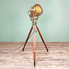 a 1984 brass industrial searchlight mounted to a hardwood tripod. This is a vintage industrial style floor lamp restored professionally and in full working order. It features a light switch on the tripod to operate the illumination