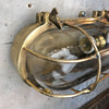 A reclaimed industrial brass oval bulkhead wall fixture with protective glass and cage.