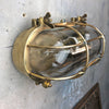 A reclaimed industrial brass oval bulkhead wall fixture with protective glass and cage.
