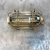 A reclaimed industrial brass oval bulkhead wall fixture with protective glass and cage.