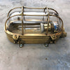 A reclaimed industrial brass oval bulkhead wall fixture with protective glass and cage.