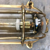 A reclaimed industrial brass oval bulkhead wall fixture with protective glass and cage.