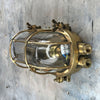 A reclaimed industrial brass oval bulkhead wall fixture with protective glass and cage.