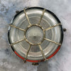A vintage industrial brass circular bulkhead wall light with target style protective cage over a prismatic glass shade.