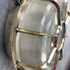 A vintage industrial brass circular bulkhead wall light with target style protective cage over a prismatic glass shade.
