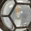 Black iron wall light with cage and prismatic glass cover. The round bulkhead is reclaimed and restored for modern interiors compatible with LED light bulb.
