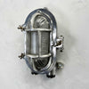 A reclaimed cast aluminium oval bulkhead wall light with a prismatic glass cover and protective cage.