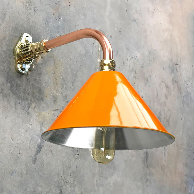 An orange cantilever wall light with copper and brass wall fixture. The orange lamp shade is based on the design of the British military festoon shades. Colourful industrial style wall lights for contemporary interiors.