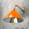 An orange cantilever wall light with copper and brass wall fixture. The orange lamp shade is based on the design of the British military festoon shades. Colourful industrial style wall lights for contemporary interiors. 
