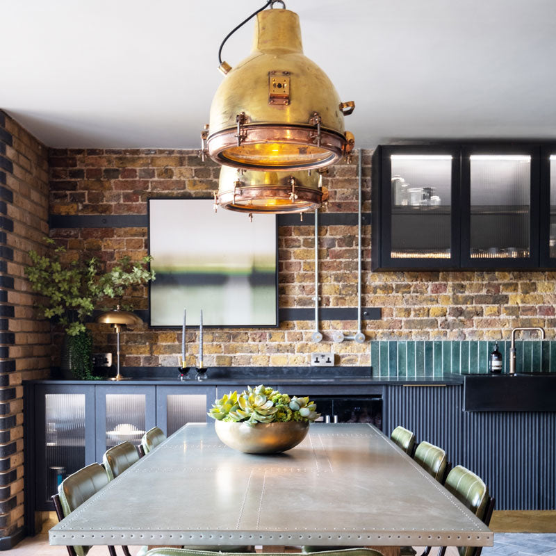 Original industrial brass hanging lights over dining table in an industrial style loft apartment kitchen diner. 