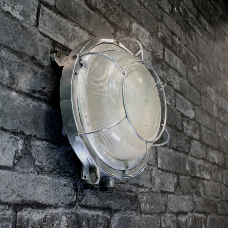 A retro industrial caged aluminium bulkhead wall light with frosted glass and protective cage.