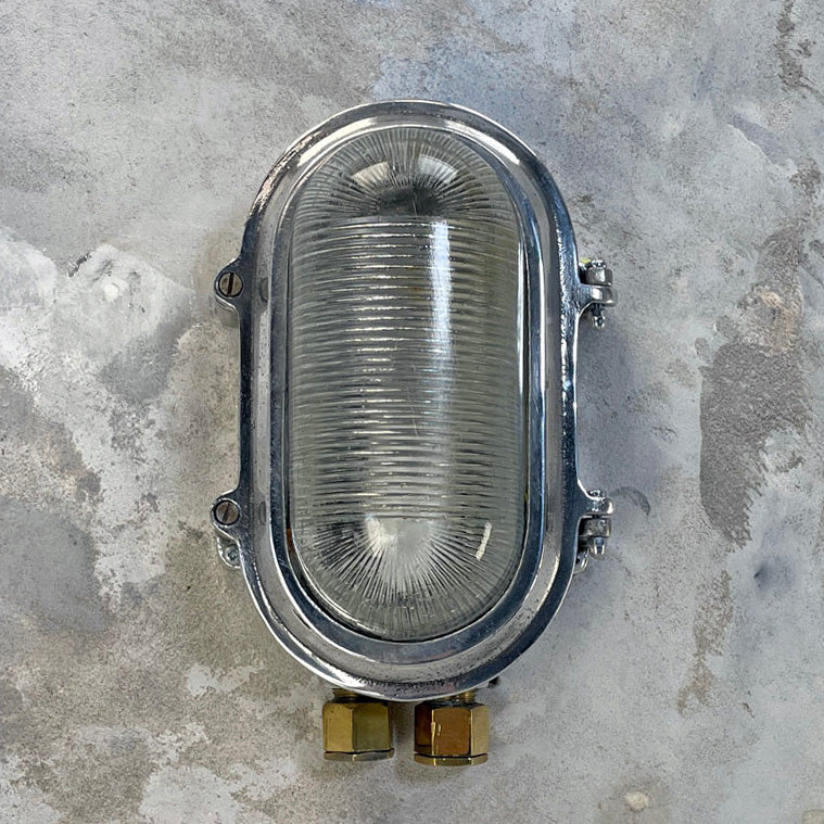 Aluminium bulkhead light for modern interiors. Our industrial wall sconce is rewired compatible with LED light bulbs. With a prismatic glass cover which softens the illumination