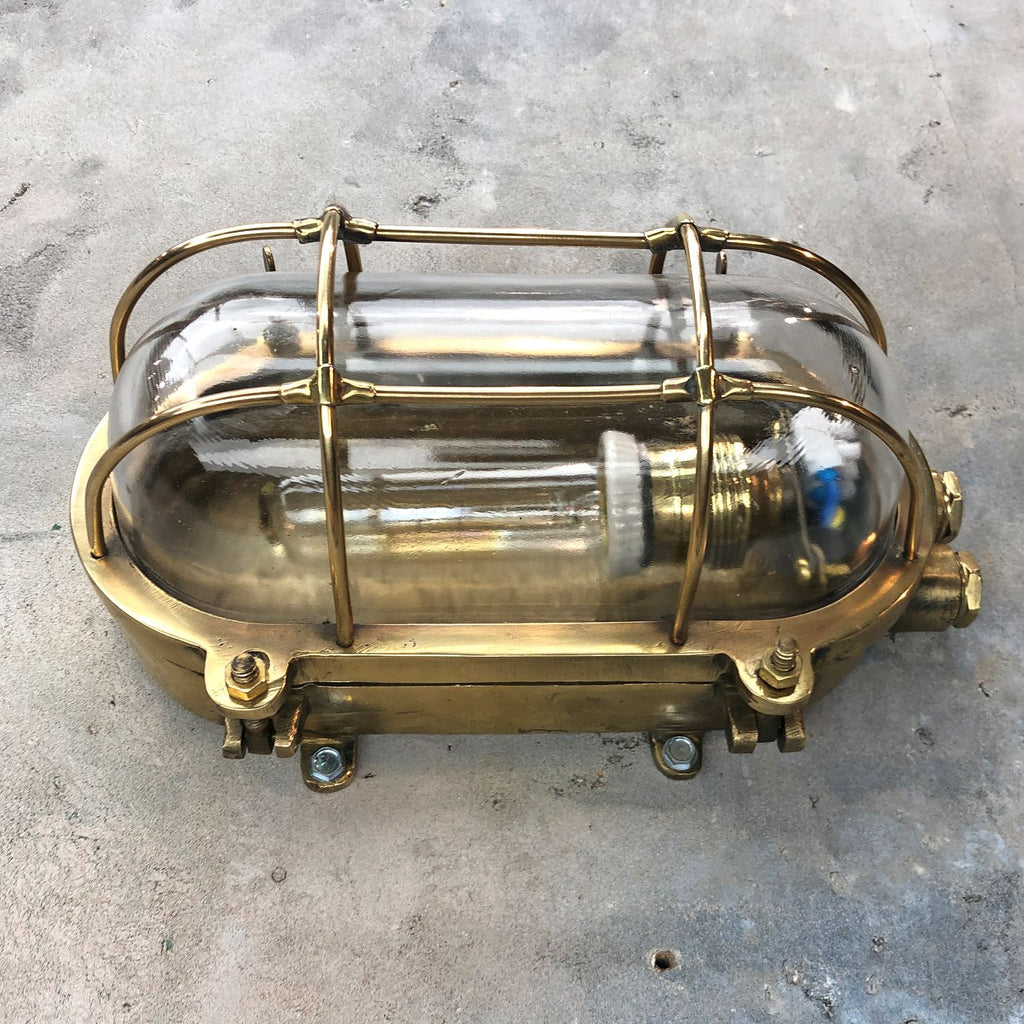 A reclaimed industrial brass oval bulkhead wall fixture with protective glass and cage.