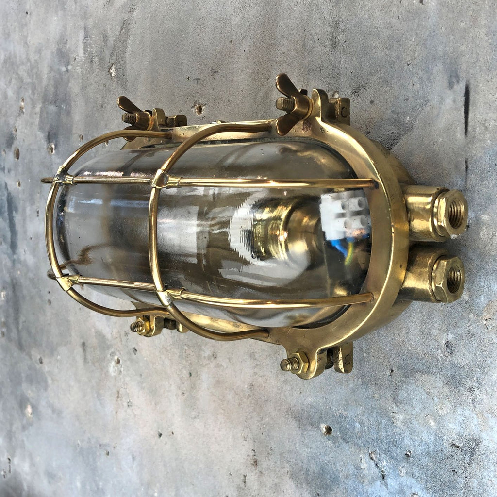 A reclaimed industrial brass oval bulkhead wall fixture with protective glass and cage.