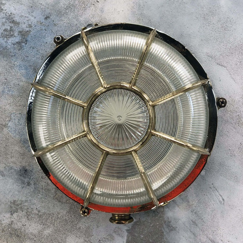 A vintage industrial brass circular bulkhead wall light with target style protective cage over a prismatic glass shade. 