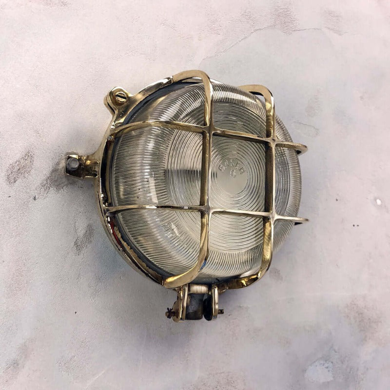 a vintage brass circular bulkhead wall light with prismatic glass shade and industrial cage