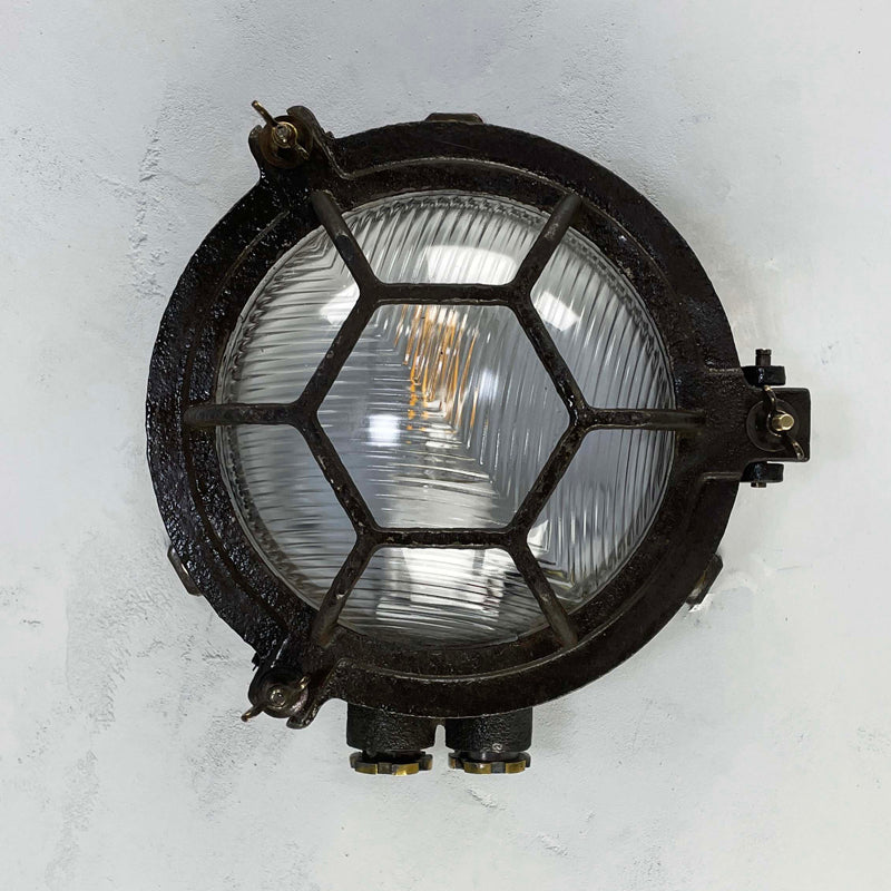 Black iron wall light with cage and prismatic glass cover. The round bulkhead is reclaimed and restored for modern interiors compatible with LED light bulb. 