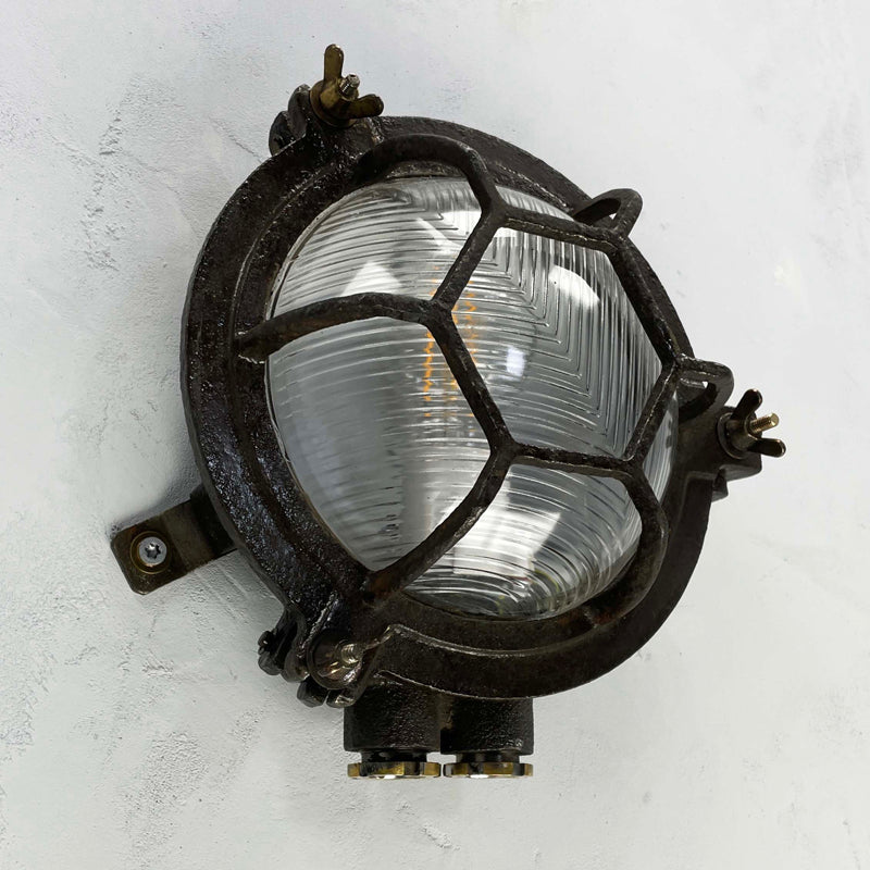 Black iron wall light with cage and prismatic glass cover. The round bulkhead is reclaimed and restored for modern interiors compatible with LED light bulb. 