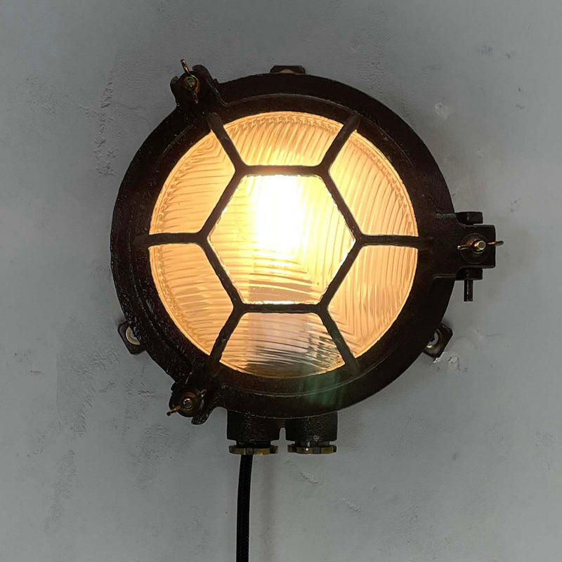 Black iron wall light with cage and prismatic glass cover. The round bulkhead is reclaimed and restored for modern interiors compatible with LED light bulb. 