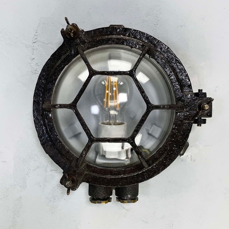 Vintage industrial black cast iron circular bulkhead wall lighting with a hexagonal target cage and clear glass dome.