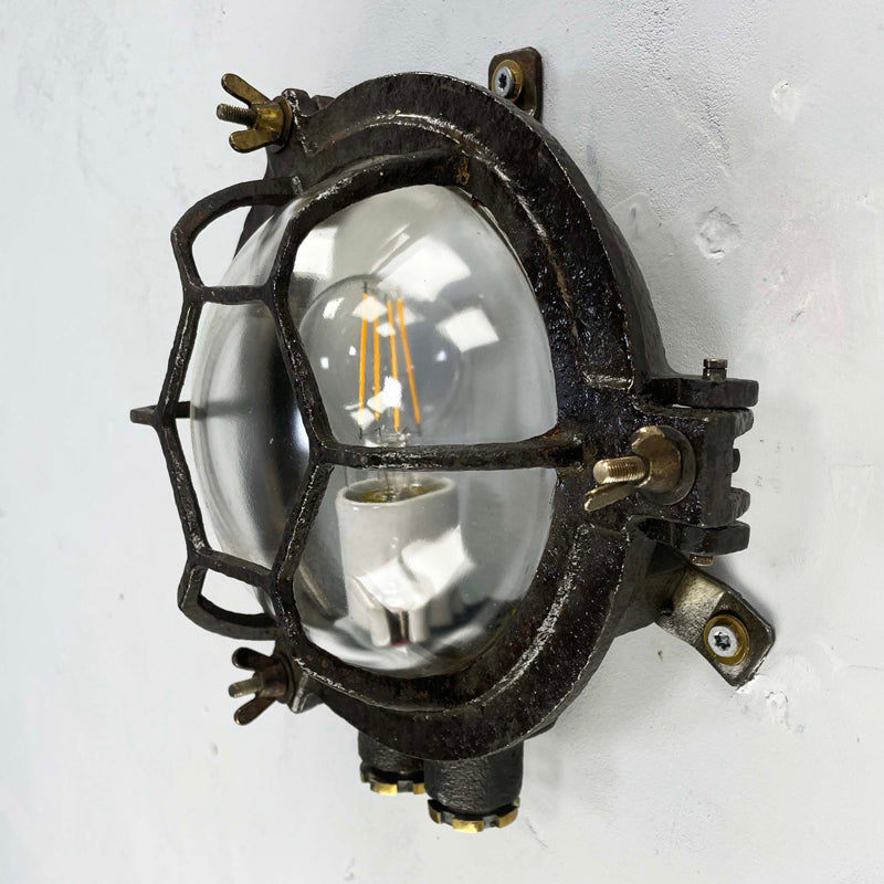 Vintage industrial black cast iron circular bulkhead wall lighting with a hexagonal target cage and clear glass dome.