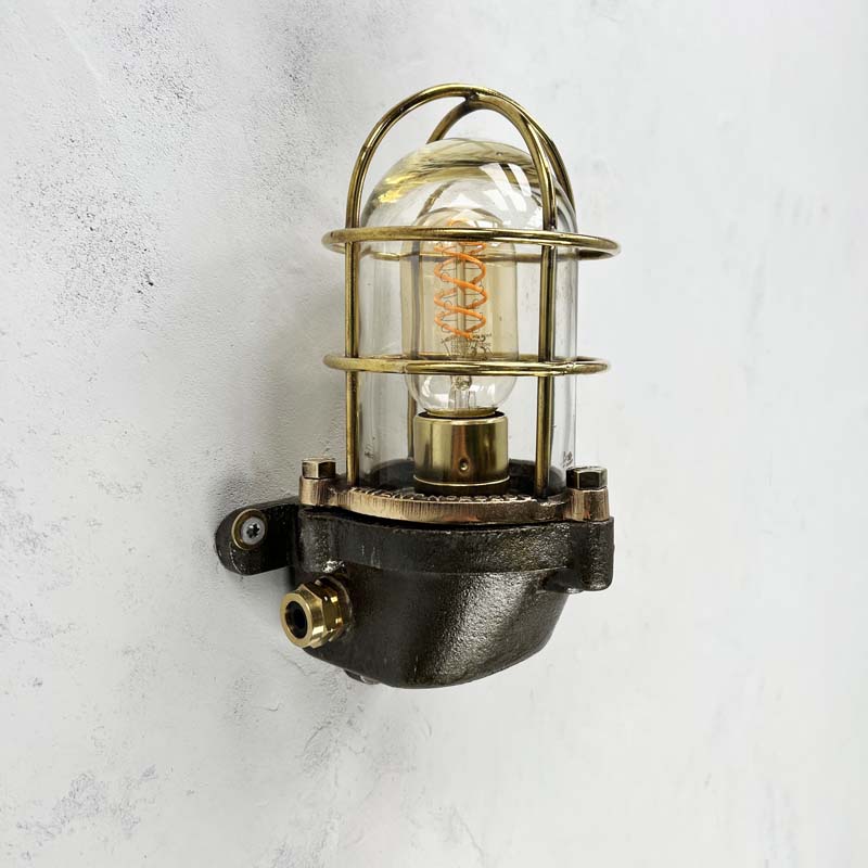 This robust industrial cage wall light manufactured C1995, comprises a cast steel main body, a tempered glass dome with a protective brass and bronze cage. 