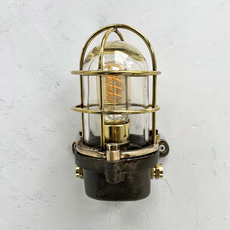 This robust industrial cage wall light manufactured C1995, comprises a cast steel main body, a tempered glass dome with a protective brass and bronze cage. 