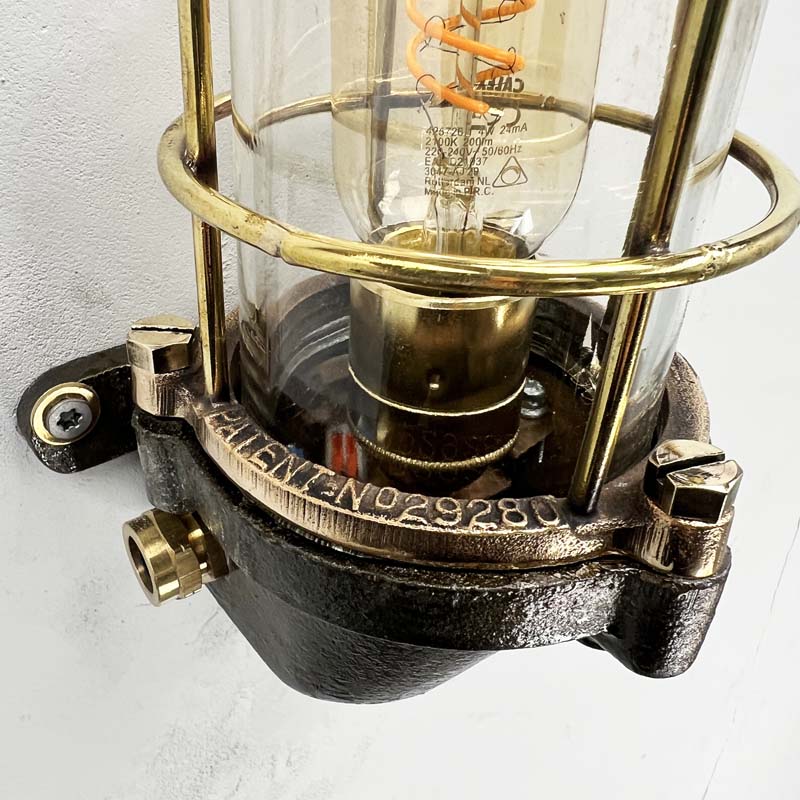 This robust industrial cage wall light manufactured C1995, comprises a cast steel main body, a tempered glass dome with a protective brass and bronze cage. 