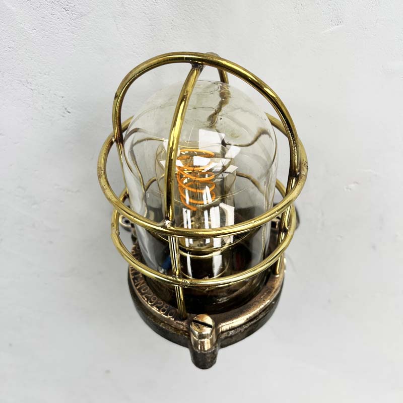 This robust industrial cage wall light manufactured C1995, comprises a cast steel main body, a tempered glass dome with a protective brass and bronze cage. 
