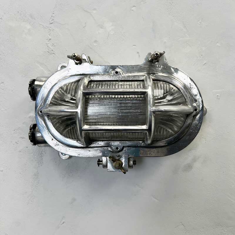 A reclaimed cast aluminium oval bulkhead wall light with a prismatic glass cover and protective cage. 