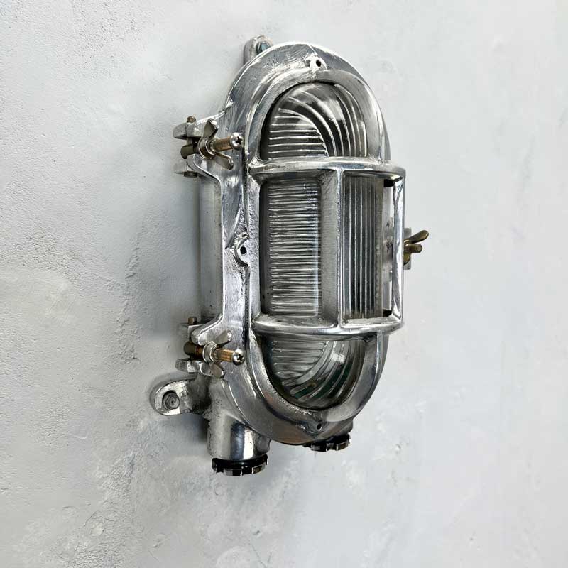 A reclaimed cast aluminium oval bulkhead wall light with a prismatic glass cover and protective cage. 