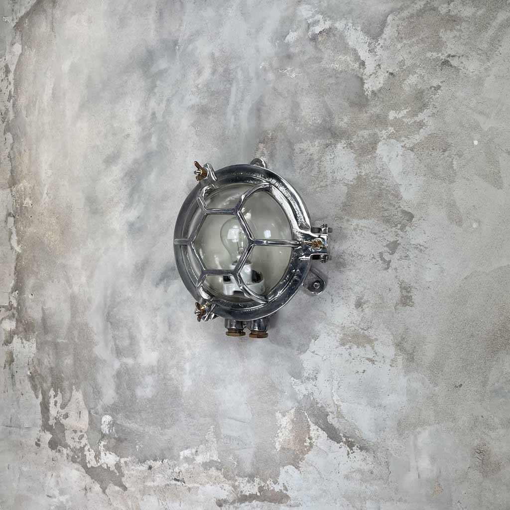 A vintage industrial aluminium outdoor circular bulkhead wall light with a hexagonal target cage and clear glass. 