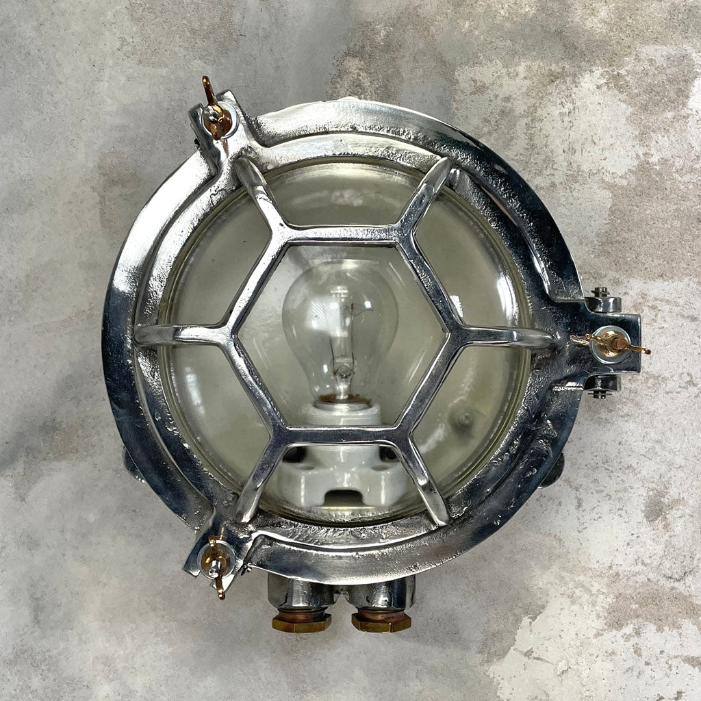 A vintage industrial aluminium outdoor circular bulkhead wall light with a hexagonal target cage and clear glass. 