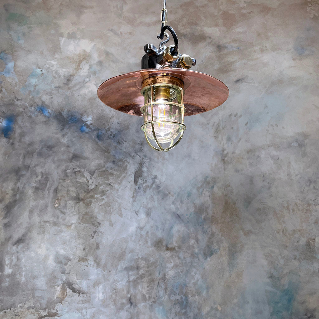 A reclaimed vintage industrial explosion proof iron and copper ceiling pendant light with a protective brass cage.