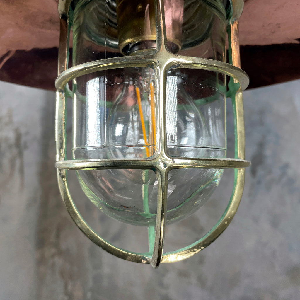 A reclaimed vintage industrial explosion proof iron and copper ceiling pendant light with a protective brass cage.